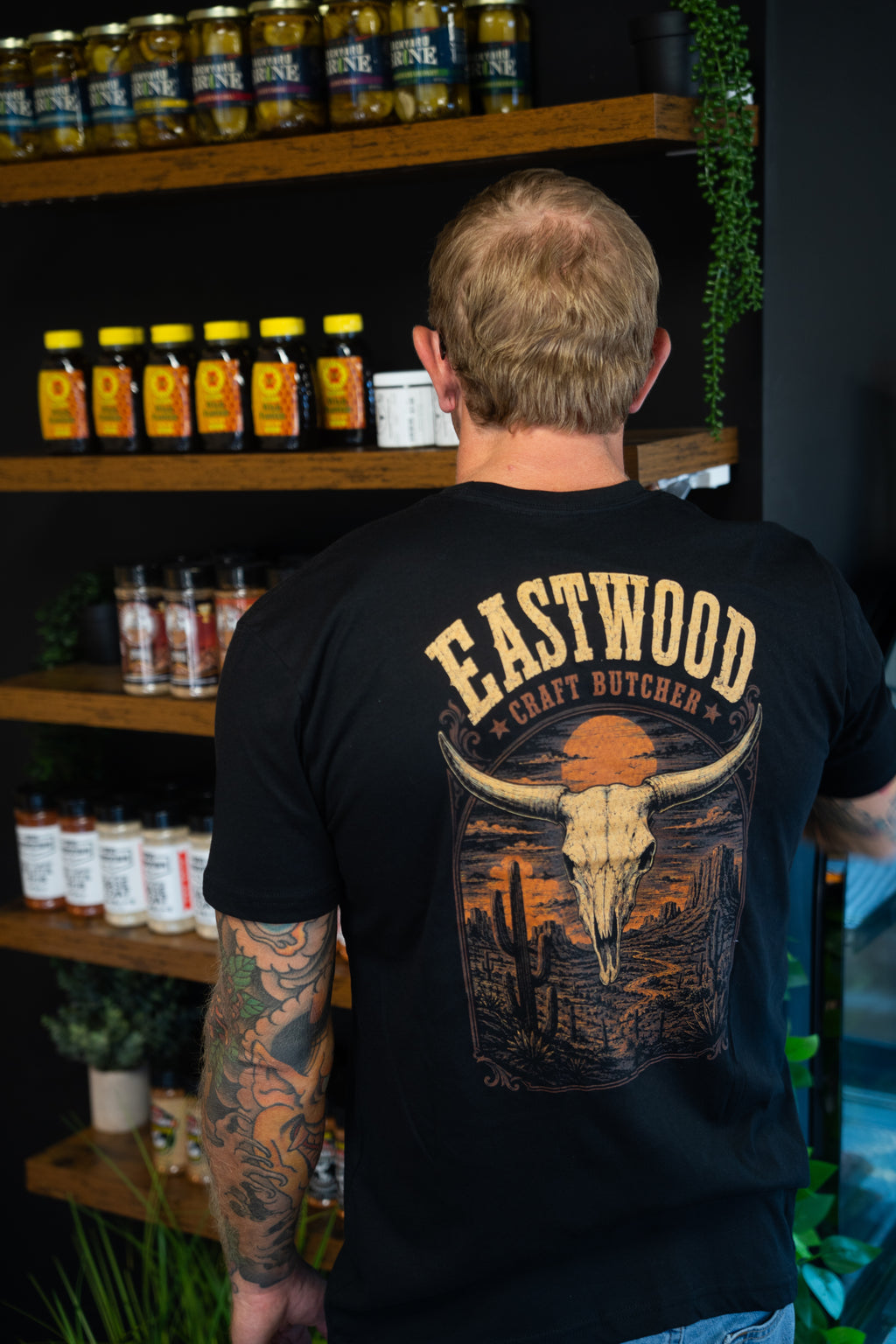 Back of black Eastwood Craft Butcher T-shirt featuring a longhorn skull, cacti, and orange desert sunset