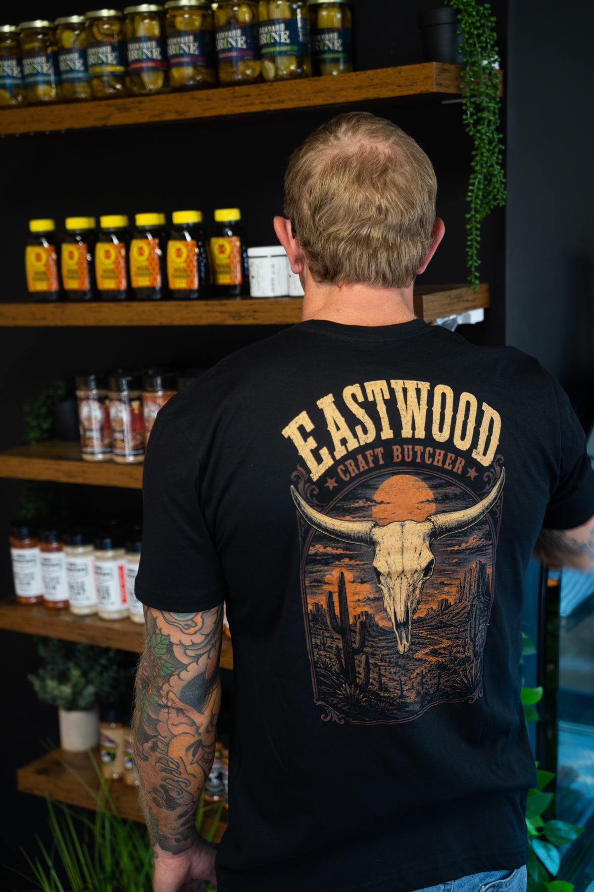 Back of black Eastwood Craft Butcher T-shirt featuring a longhorn skull, cacti, and orange desert sunset